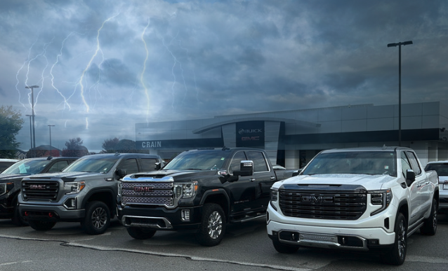 Row of GMC trucks parked at Crain Buick GMC in Springdale with storm clouds and lightning in the background